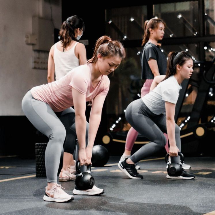 네 명의 여성이 체육관에서 케틀벨을 들고 운동하고 있다.