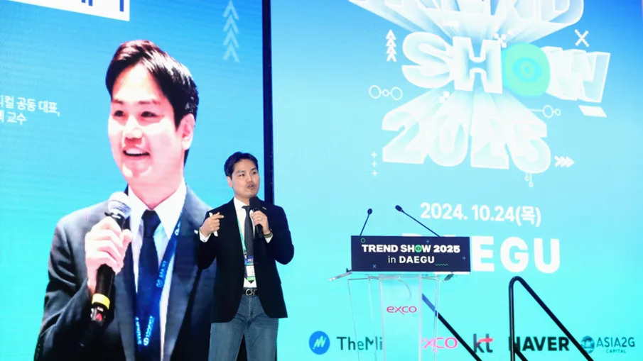 한 남성이 무대에서 마이크를 들고 발표하고 있으며, 뒤에는 'TREND SHOW 2025'와 '2024.10.24(목) DAEGU' 등의 글씨가 쓰인 대형 스크린이 있다.