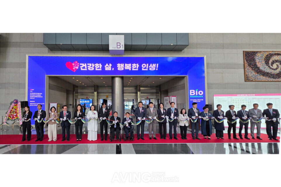 여러 명의 사람들이 전시장 입구에서 리본을 자르는 개막식 장면. 배경에는 '건강한 삶, 행복한 인생!'이라는 문구와 바이오 헬스케어 관련 안내판이 보임.