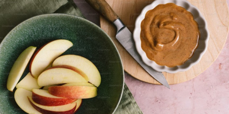 녹색 그릇에 담긴 사과 슬라이스와 옆에 놓인 땅콩버터, 그리고 작은 나이프가 있는 장면