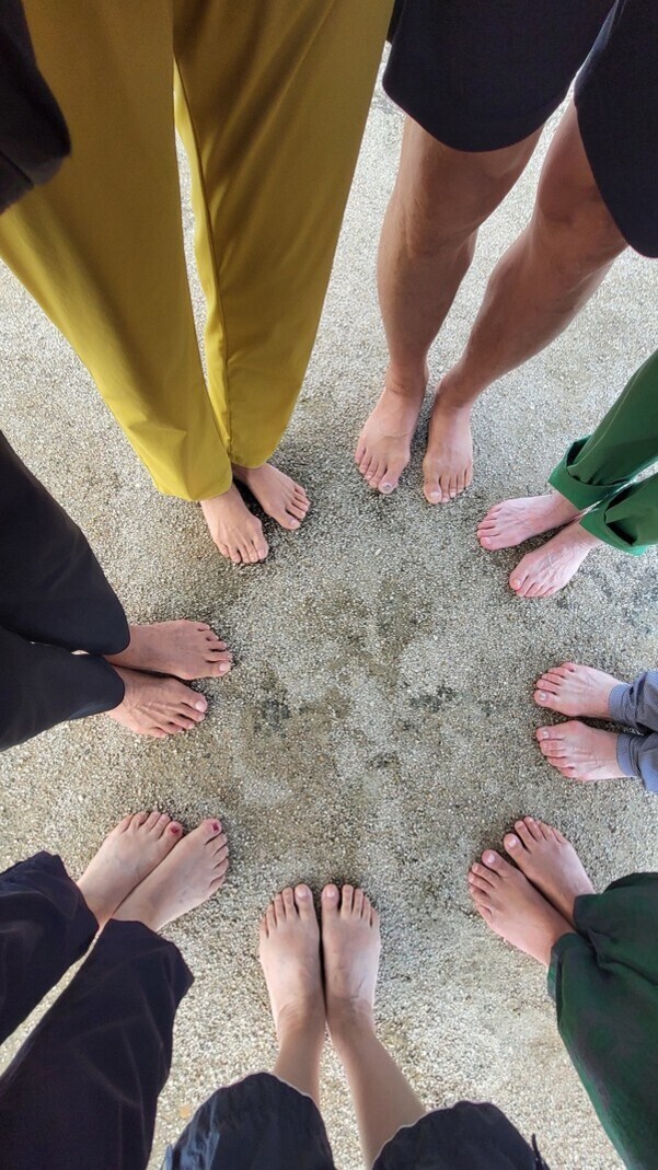 여러 명이 맨발로 모래 위에 원을 이루며 서 있는 모습
