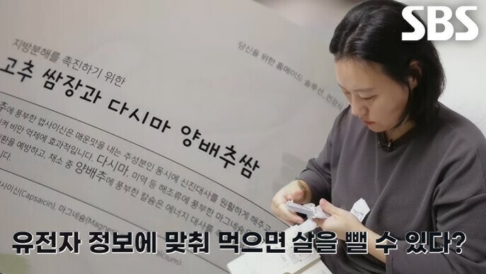 한 여성이 테이블에 앉아 무언가를 보고 있으며, 벽에는 '고추 쌈장과 다시마 양배추쌈'이라는 글씨와 설명이 적혀 있다. 화면 오른쪽 위에 SBS 로고가 있고, 하단에는 '유전자 정보에 맞춰 먹으면 살을 뺄 수 있다?'라는 자막이 보인다.