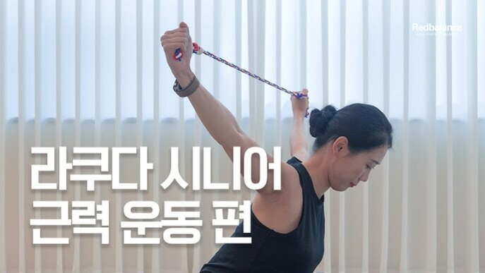 여성이 실내에서 탄력 밴드를 이용해 팔 근력 운동을 하고 있으며, 화면에 '라쿠다 시니어 근력 운동 편'이라는 문구가 적혀 있다.