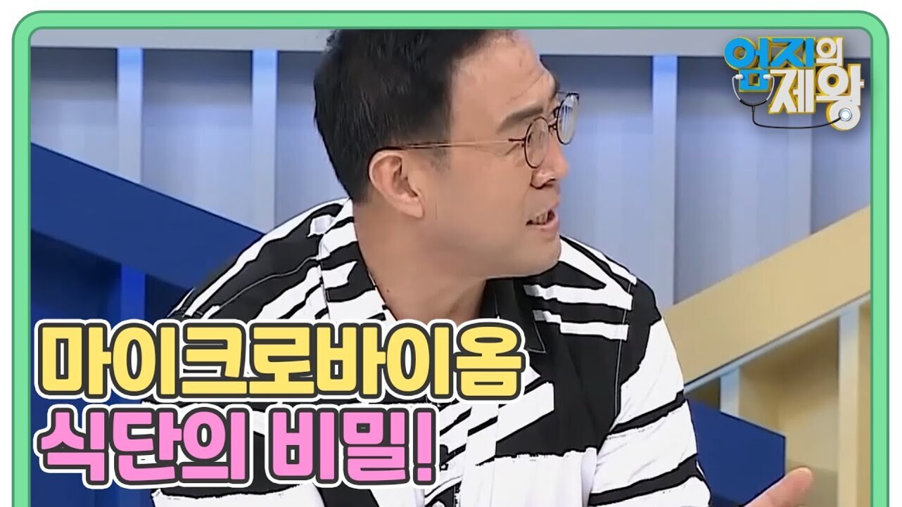 안경을 쓴 남성이 검정과 흰색 줄무늬 옷을 입고 토크쇼 세트장에서 대화하고 있다. 화면에는 '마이크로바이옴 식단의 비밀!'이라는 문구가 적혀 있다.