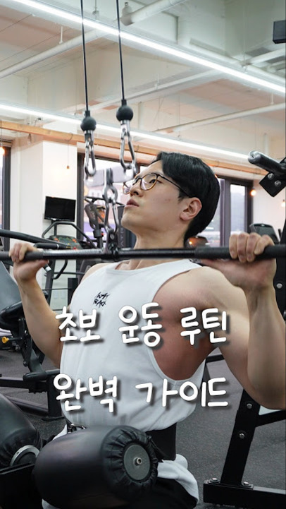 헬스장에서 안경을 쓴 남성이 랫풀다운 운동 기구를 이용해 등 운동을 하고 있으며, 화면 중앙에는 '초보 운동 루틴 완벽 가이드'라는 문구가 적혀 있다.