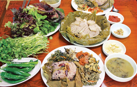여러 종류의 쌈채소, 고추, 나물 반찬, 된장국, 마늘과 쌈장 등의 밑반찬 그리고 연잎밥과 수육이 상 위에 차려진 한식 정식 상차림