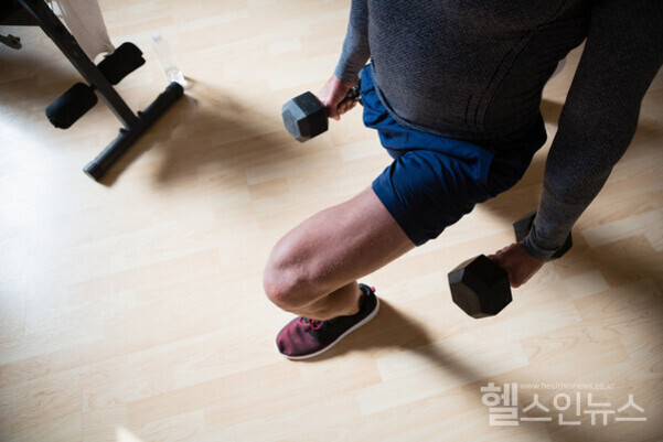 남성이 양손에 아령을 들고 런지 운동을 하는 모습