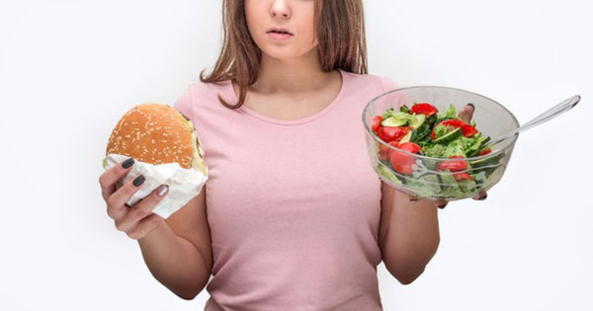 여성이 한 손에는 햄버거를, 다른 손에는 샐러드가 담긴 그릇을 들고 있다.