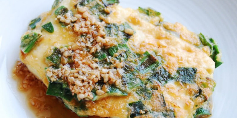 파와 깨가 올려진 계란찜이 흰 접시에 담겨 있다.