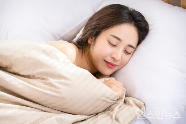 여성이 침대에 누워 포근하게 이불을 덮고 편안하게 잠들어 있다.