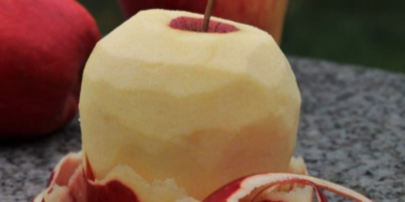 껍질이 벗겨진 사과와 그 주변에 감긴 사과 껍질, 배경에는 다른 사과들이 놓여 있다.