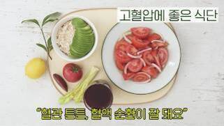 접시에 오트밀, 아보카도, 토마토와 양파 샐러드가 담겨 있고 옆에 레몬, 토마토, 셀러리, 포도주스가 놓여 있다. 상단에는 '고혈압에 좋은 식단'이라는 문구가 있고 하단에는 '혈관 튼튼, 혈액 순환이 잘 돼요'라는 문구가 있다.