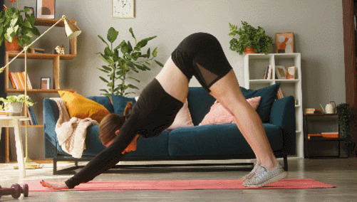 여성이 거실에서 요가 매트 위에 다운독 자세로 운동하고 있다.