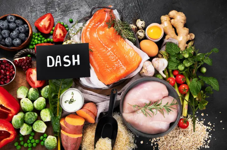 생연어, 닭가슴살, 다양한 채소와 과일(브로콜리, 방울토마토, 블루베리, 고구마 등), 곡물 및 계란이 진열되어 있고 'DASH'라고 적힌 표지판이 있는 건강식 식재료 모음