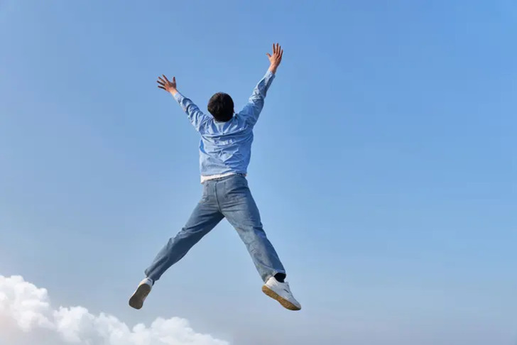 한 남성이 파란 하늘을 배경으로 점프하며 두 팔을 높이 들고 있다.